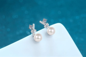 Macro detail of S925 silver bow earrings with round white pearls and pavé set zircons