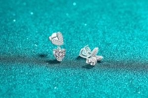 Dettaglio degli orecchini a cuore in argento S925 con fiocco su sfondo blu glitterato