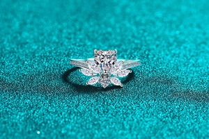 Macro detail of a silver heart moissanite ring with marquise diamonds on a blue backdrop