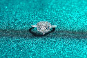 Makroaufnahme eines herzförmigen Moissanit-Rings mit Diamant-Halo auf Glitzergrund