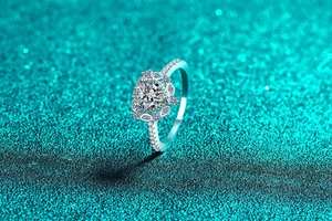 Nahaufnahme eines herzförmigen Moissanit-Rings mit Halo- und Pavé-Fassung auf Türkis