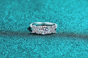 Macro shot of silver ring with Moissanite stones and flower cluster setting on teal surface