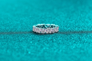 Close-up of S925 silver eternity ring with baguette and round moissanite on teal background