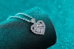 Macro shot of silver heart pendant featuring a Moissanite centerpiece on a teal podium