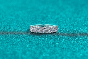 Macro shot of silver ring with five oval-cut moissanite stones on green glitter base