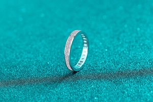 S925 sterling silver eternity ring with moissanite pavé stones on blue glitter background