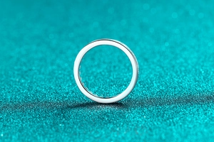 Polished silver ring with smooth metal surface on shimmering blue sequin background