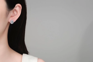 Close-up of S925 sterling silver sunburst earrings with light blue stone on model ear