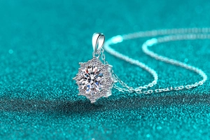 Macro shot of silver flower pendant with moissanite center stone on glittery teal backdrop