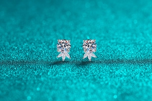 Close-up of S925 silver stud earrings with marquise-cut stones on a teal glitter background