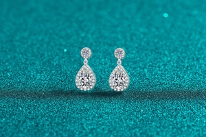 Macro view of pear-cut moissanite halo drop earrings on sparkling teal background