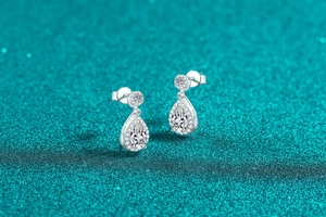 Macro detail of pear-shaped moissanite earrings with halo diamonds on teal glitter