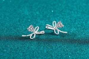 Detailed view of silver bow-knot heart earrings with moissanite on a blue-green shimmer surface