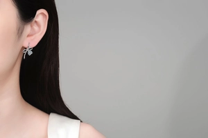 Detail view of a S925 sterling silver bow earring with a pear-shaped moissanite on model