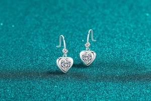 Close-up of S925 sterling silver heart-shaped moissanite drop earrings on textured background