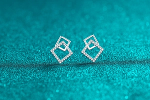 Macro di orecchini quadrati in argento S925 con moissanite su sfondo blu scintillante