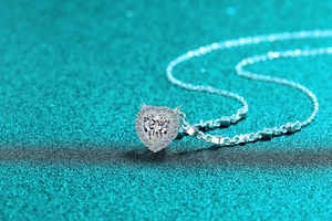 Gros plan d'un collier cœur en argent S925 et moissanite avec sertissage halo sur fond pailleté