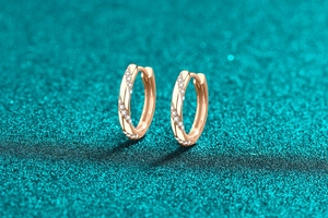 Detail of rose gold twisted hoop earrings with pavé set cubic zirconia on teal surface