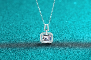 Macro shot of emerald cut moissanite pendant with halo setting on a blue glitter surface