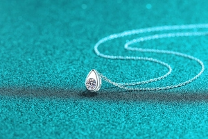 Macro shot of silver teardrop necklace pendant with sparkling center stone on blue background
