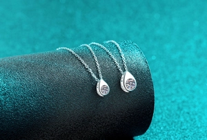 Detailed close-up of two teardrop silver necklaces with Moissanite stones on a stand