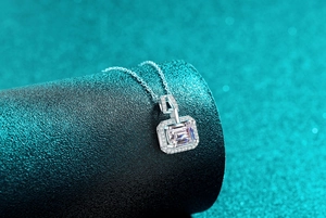 Macro shot of emerald cut moissanite pendant with halo setting on dark display stand