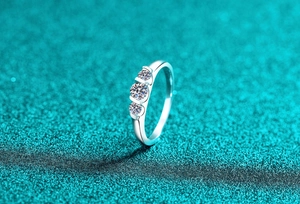 Macro shot of three-stone moissanite silver ring on sparkling teal textured background