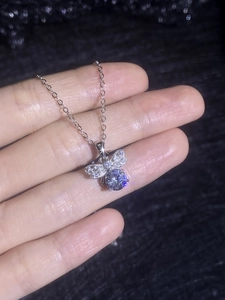 Detailed view of silver bow-knot bee pendant with sparkling moissanite gemstone held by hand