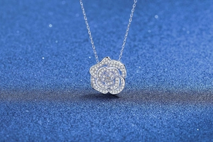 Vue détaillée d'un pendentif camélia en argent serti de moissanites sur fond bleu mat