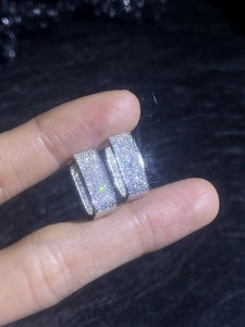 Macro shot of sparkling full moissanite pavé silver hoop earrings held by hand
