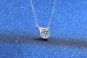 Detail of teardrop pendant necklace featuring a brilliant round cut moissanite on blue background