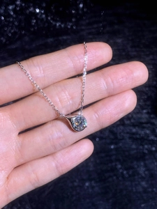 Macro shot of 1 carat round moissanite pendant with elegant silver chain on hand