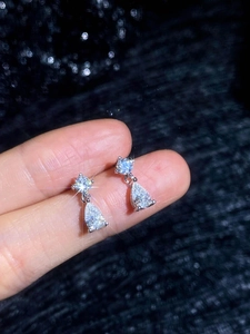 Détail de boucles d'oreilles en moissanite poire et argent S925 tenues par la main