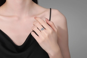Detail view of square moissanite halo ring worn on hand with elegant silk dress background