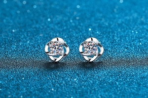 Macro shot of silver four-leaf clover moissanite earrings on a glittery blue background