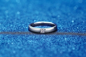 Macro shot of princess cut moissanite set in polished silver ring band on blue background
