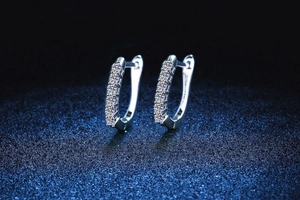 Macro shot of silver sterling huggie earrings with round moissanite rows on blue background