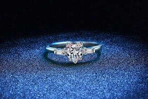 Macro view of heart-cut moissanite ring with baguette side stones on blue background