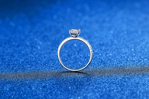 Close-up of S925 sterling silver ring featuring emerald cut moissanite on blue background