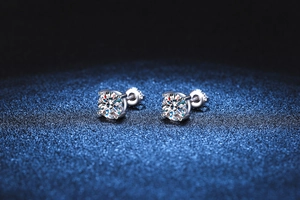 Macro shot of 4-prong moissanite stud earrings on deep blue sparkling background