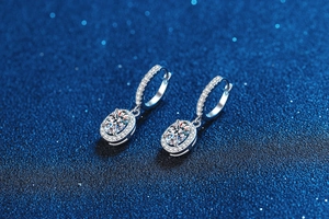 Macro shot of oval cut moissanite drop earrings with halo setting on a blue background