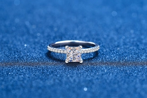 Macro shot of princess cut moissanite ring with pavé diamonds on a blue background