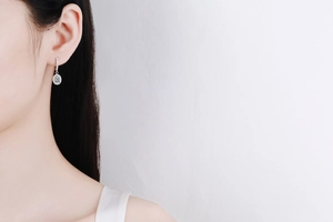 Close-up of classic silver moissanite drop earrings worn by model on white background