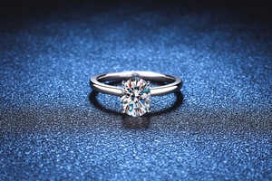 Macro detail of oval cut moissanite ring in silver four-prong setting on blue background