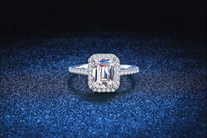 Vista macro di un anello in moissanite taglio smeraldo con halo su sfondo blu navy testurizzato