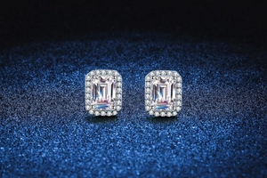 Macro view of emerald-cut Moissanite stud earrings with halo setting on glitter background