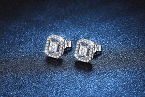 Macro shot of silver moissanite earrings with halo set emerald cut stones