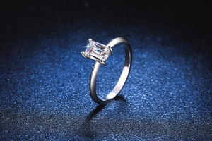 Close-up of emerald cut moissanite ring with four-prong setting on dark blue background