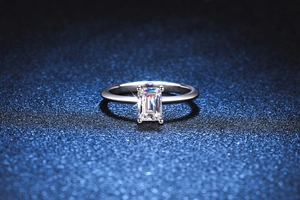Macro shot of emerald cut moissanite ring with four-prong setting on blue background
