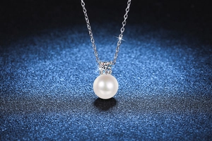 Macro view of a round white pearl pendant with a brilliant moissanite stone on a silver chain